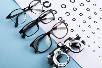 Photo of Vision test chart, glasses and trial frame on light blue background