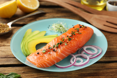 Photo of Delicious fresh salmon with spinach, avocado and onion served on wooden table