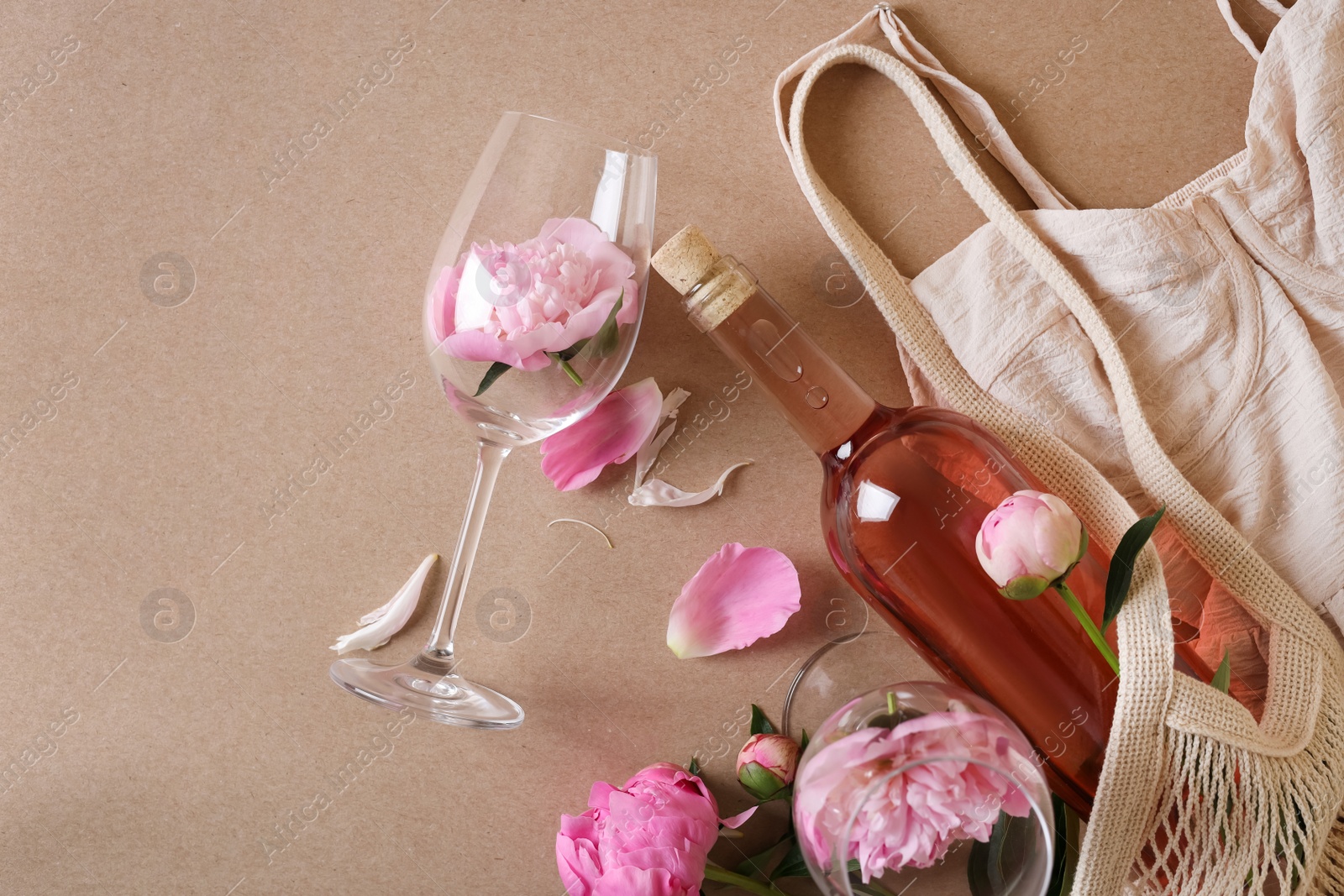 Photo of Flat lay composition with rose wine, mesh bag, dress and beautiful pink peonies on brown background