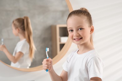 Photo of Cute little girl holding plastic toothbrush in bathroom, space for text