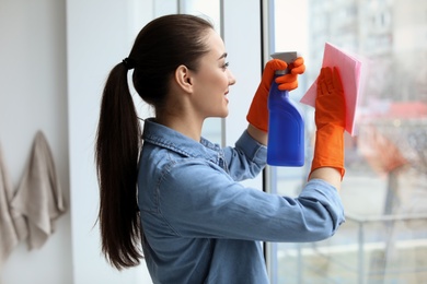 Photo of Young woman cleaning window glass at home