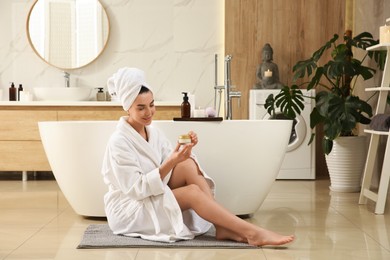 Beautiful young woman with jar of cream near tub in bathroom