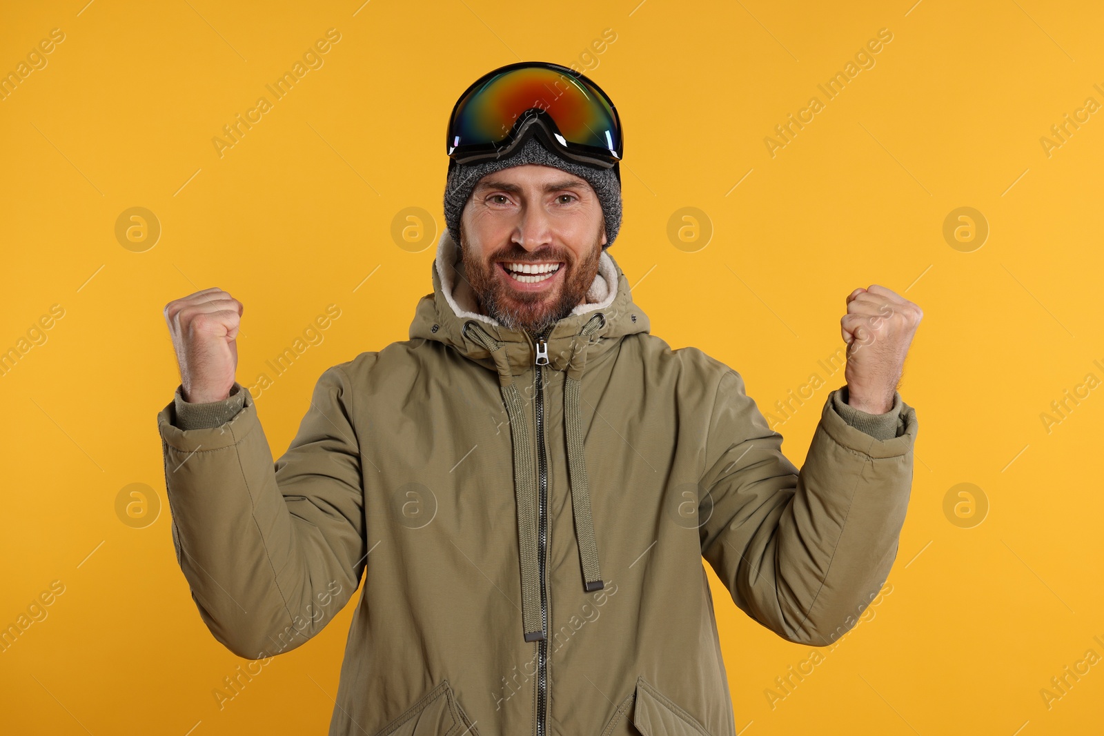 Photo of Winter sports. Cheerful man in ski suit and goggles on orange background