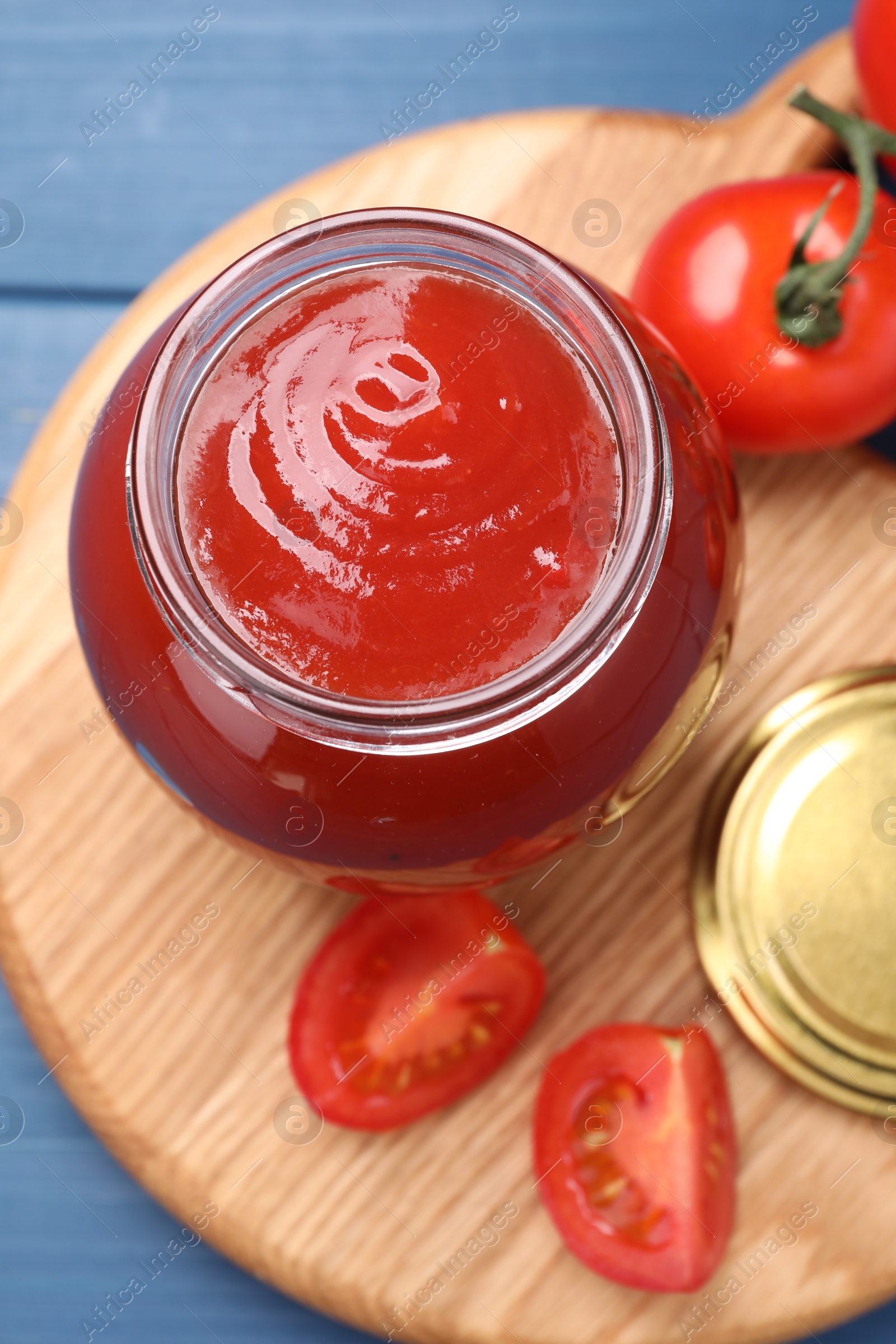 Photo of Organic ketchup in jar and fresh tomatoes on blue table, top view. Tomato sauce