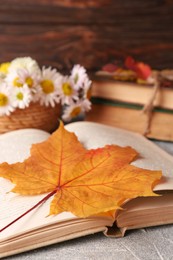 Book with autumn leaf as bookmark on light gray textured table, closeup