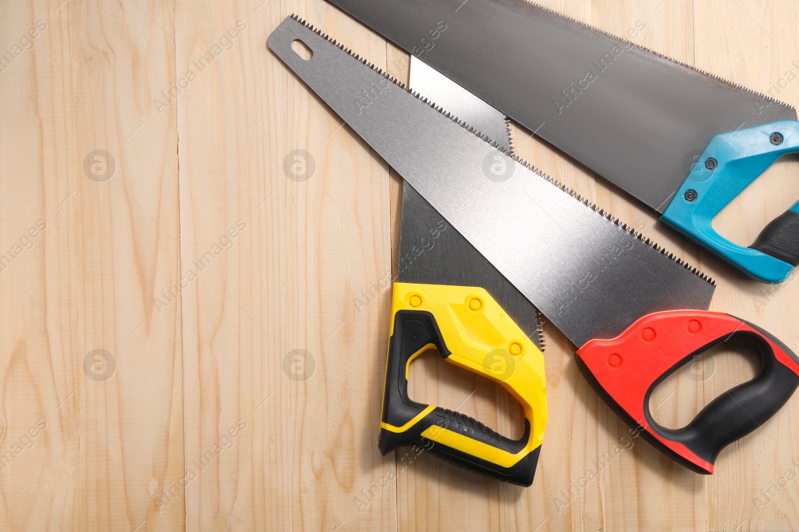 Photo of Saws with colorful handles on wooden background, flat lay. Space for text