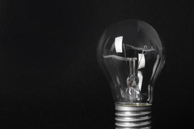 New modern lamp bulb on black background, space for text