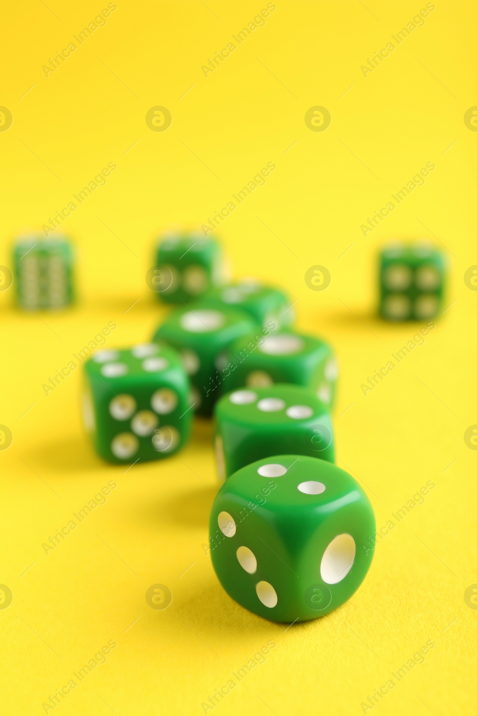 Photo of Many green game dices on yellow background, closeup