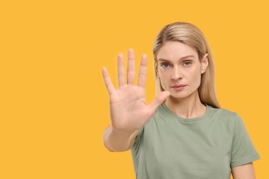 Photo of Woman showing stop gesture on yellow background. Space for text