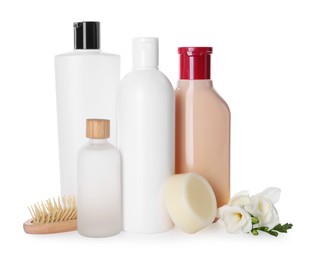Different bottles of shampoo and wooden brush on white background