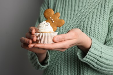Photo of Woman holding tasty cupcake with gingerbread man cookie on light background, closeup. Christmas celebration