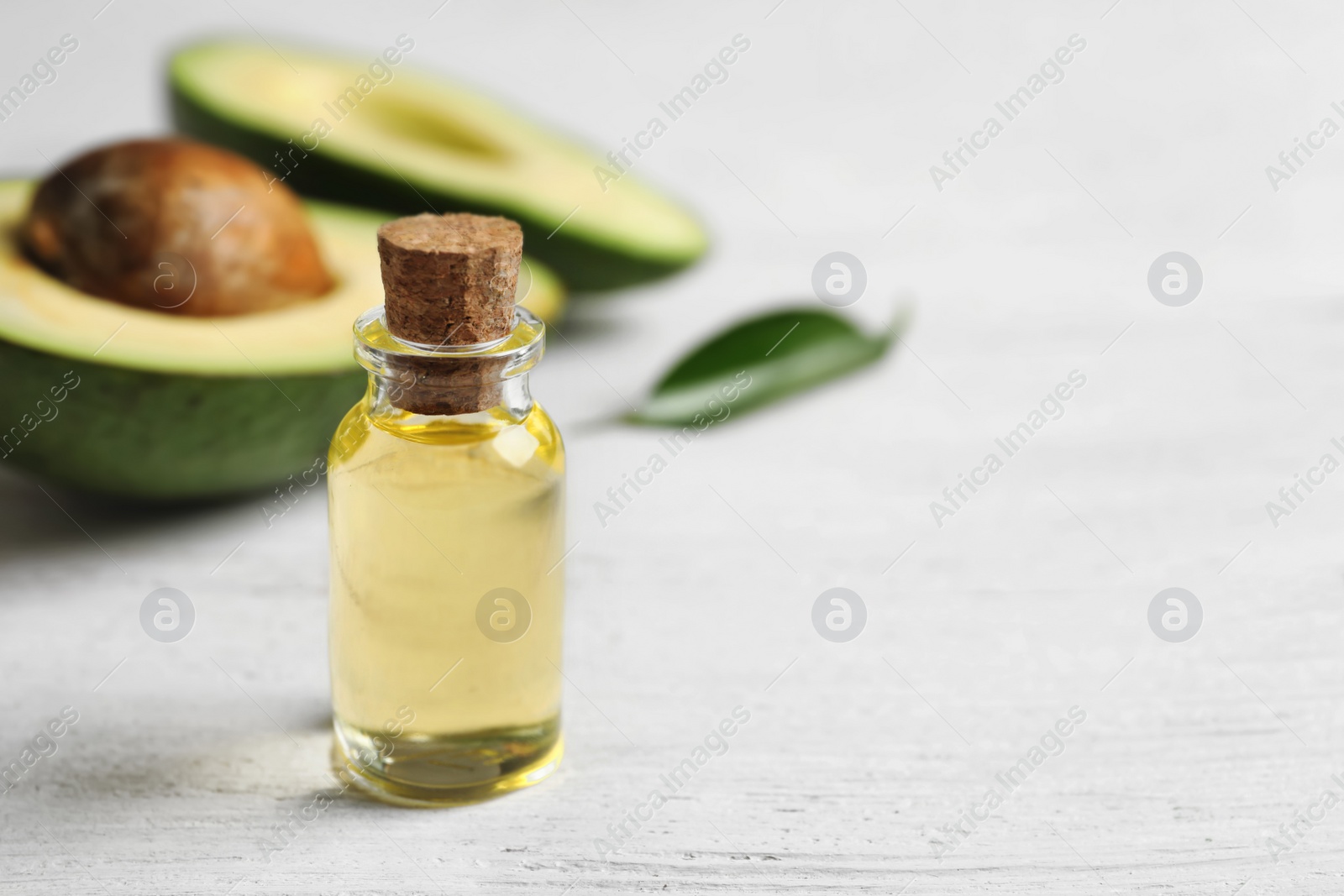 Photo of Bottle with oil and fresh avocado on wooden table