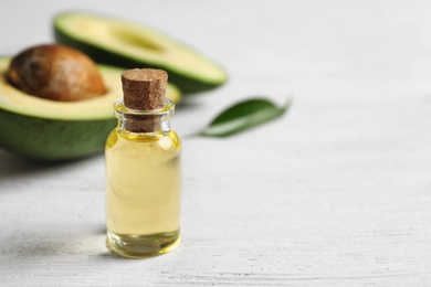 Photo of Bottle with oil and fresh avocado on wooden table