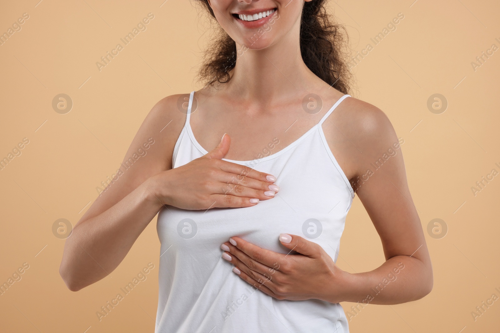 Photo of Woman doing breast self-examination on light brown background, closeup