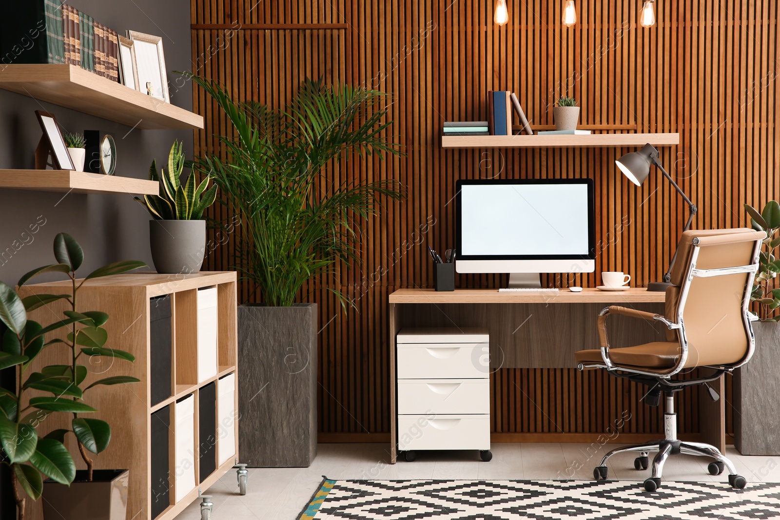 Photo of Comfortable workplace with computer near wooden wall in stylish room interior. Home office design