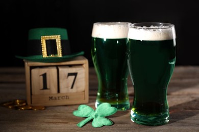 Photo of St. Patrick's day celebrating on March 17. Green beer, block calendar, leprechaun hat, gold coins and decorative clover leaf on wooden table