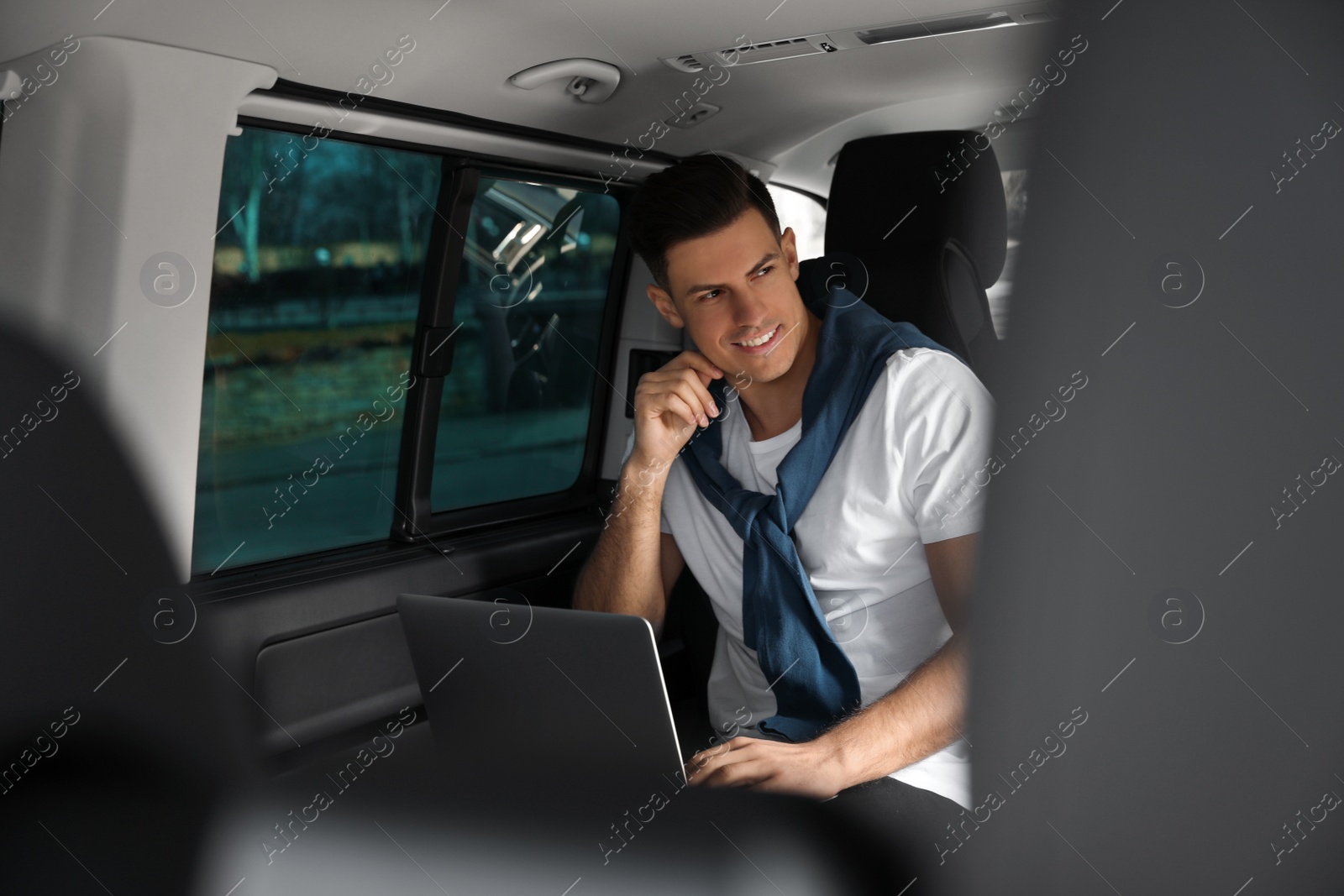 Photo of Handsome man working with laptop on backseat of modern car