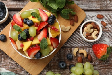 Tasty fruit salad in bowl and ingredients on wooden table, flat lay