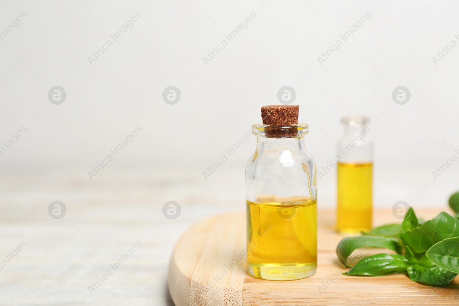 Photo of Wooden board with glass bottles of basil oil,leaves and space for text