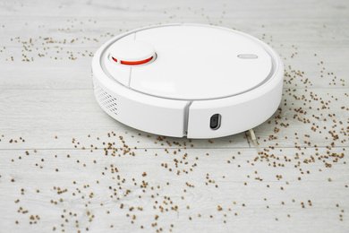 Removing groats from wooden floor with robotic vacuum cleaner at home, closeup