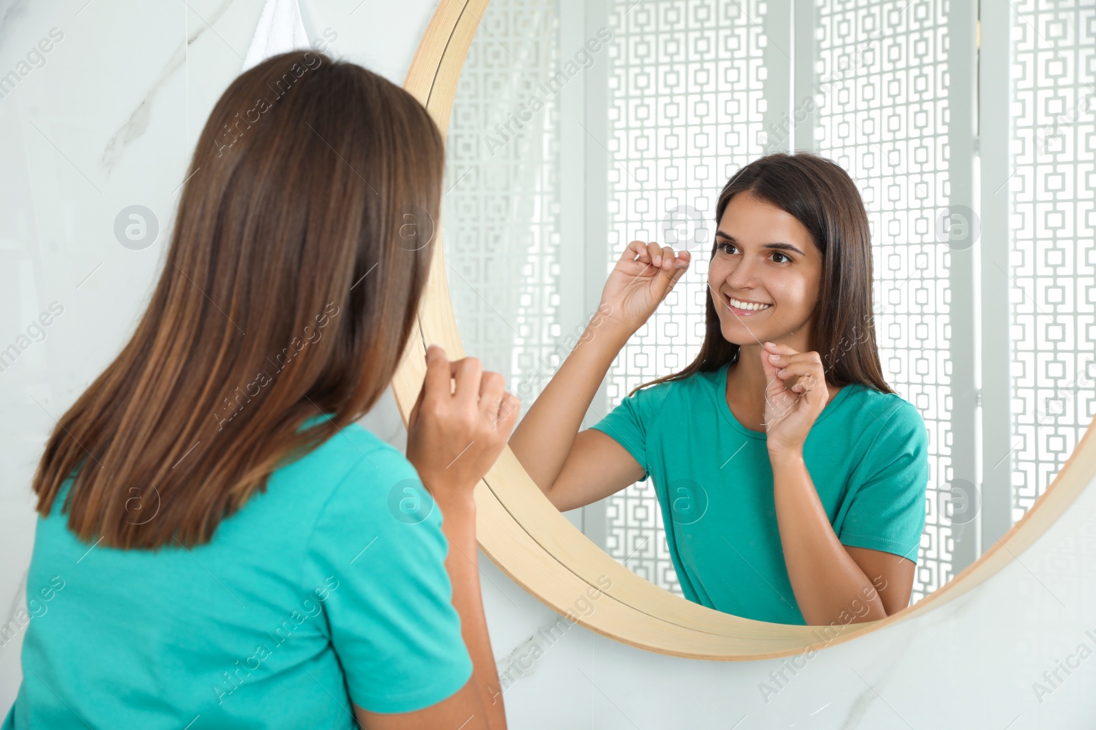 Photo of Young woman flossing her teeth in bathroom. Cosmetic dentistry