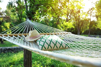 Comfortable net hammock with pillow and hat hanging in green garden