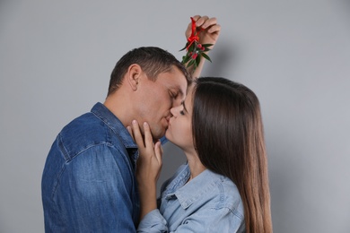 Photo of Happy couple kissing under mistletoe bunch on grey background