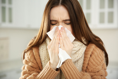 Photo of Sick young woman sneezing at home. Influenza virus