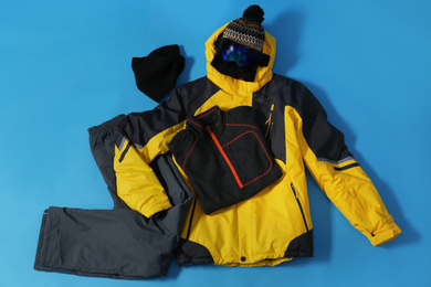 Stylish winter sport clothes on light blue background, flat lay