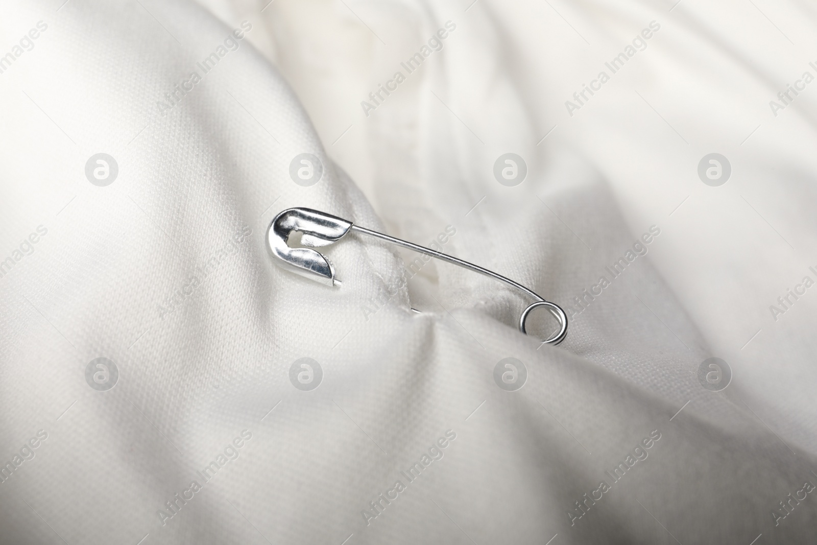 Photo of Metal safety pin on white fabric, closeup