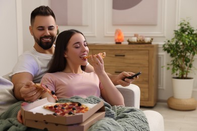 Photo of Happy young couple watching tv and eating pizza on sofa in living room. Space for text