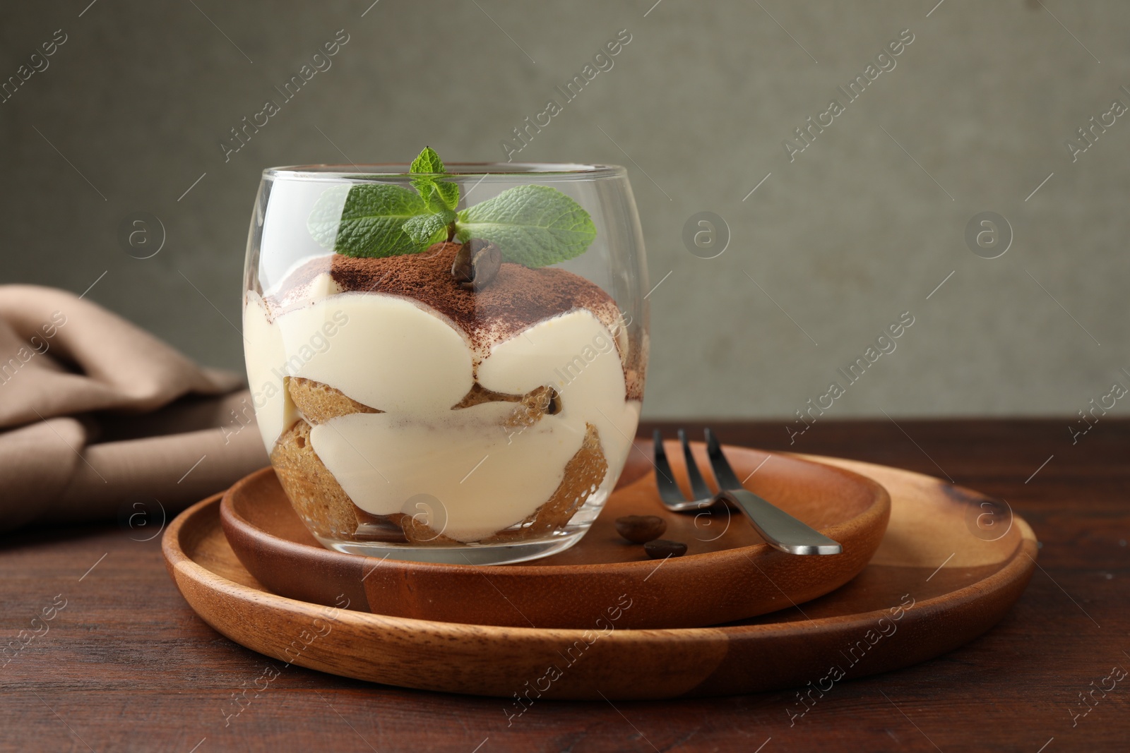 Photo of Delicious tiramisu in glass, mint leaves, coffee beans and fork on wooden table