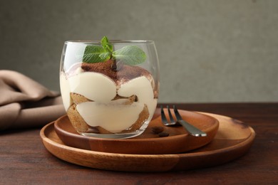 Delicious tiramisu in glass, mint leaves, coffee beans and fork on wooden table