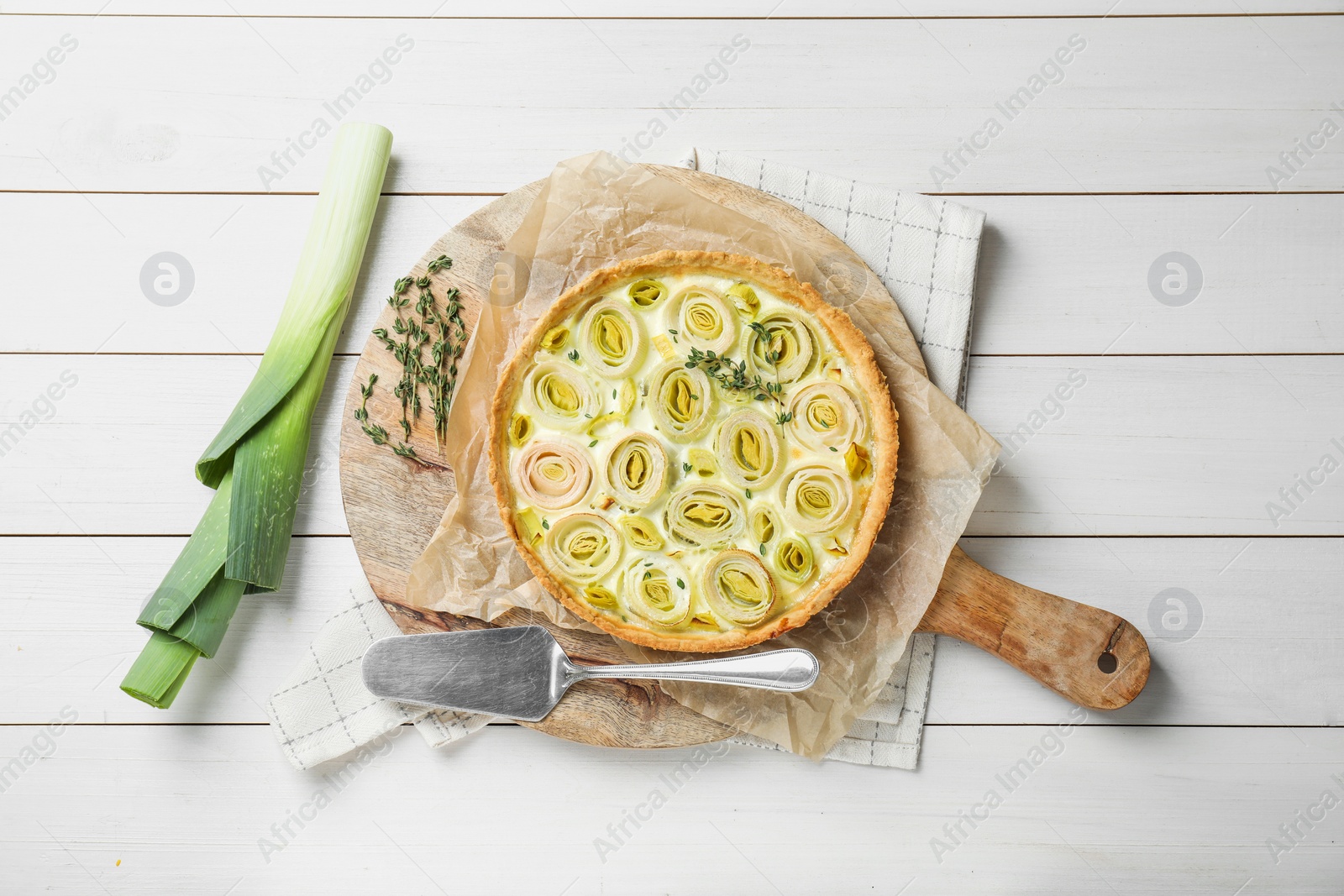 Photo of Tasty leek pie, thyme and fresh stalk on white wooden table, flat lay