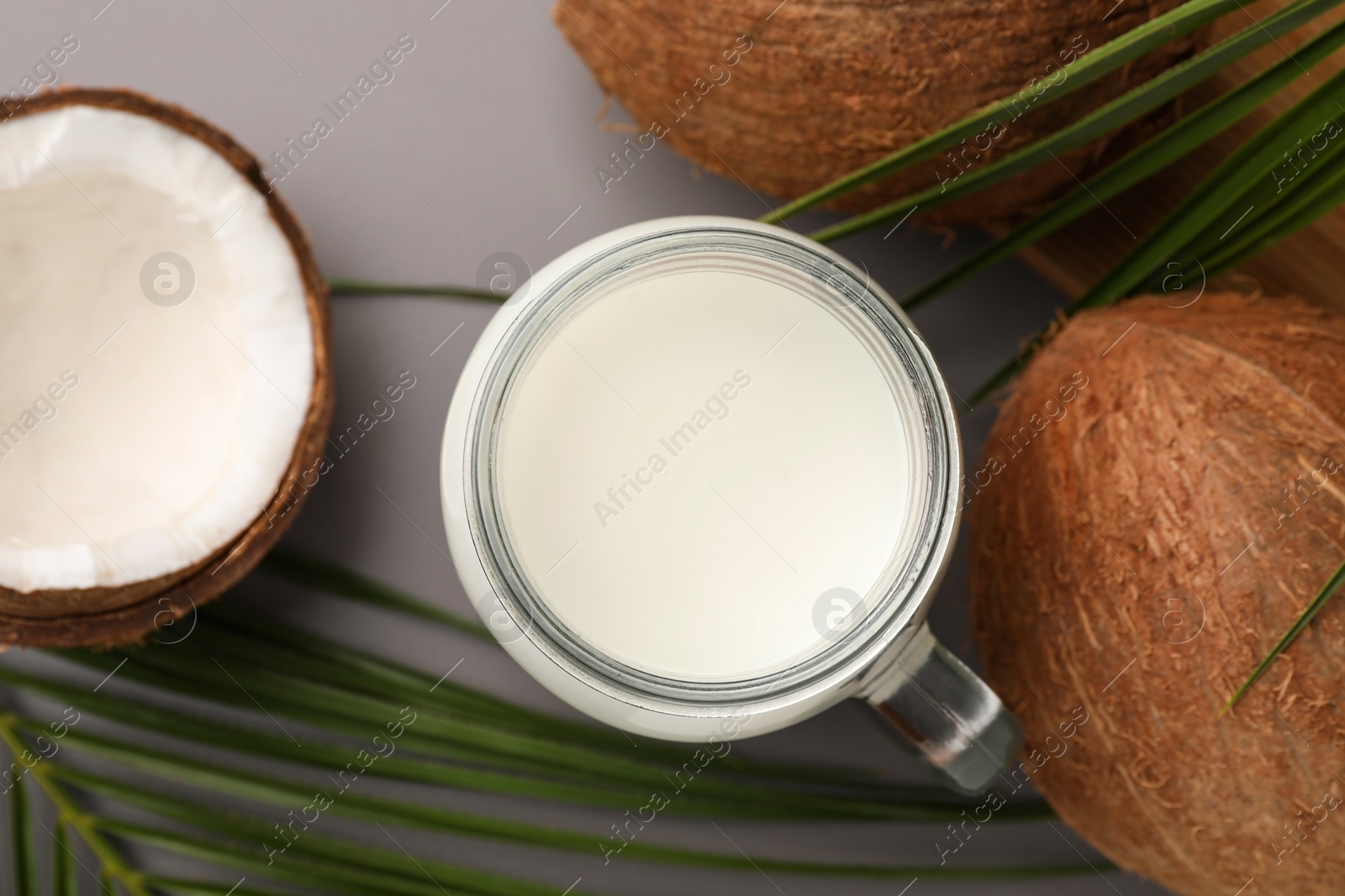 Photo of Mason jar of delicious vegan milk, coconuts and leaves on grey background, flat lay