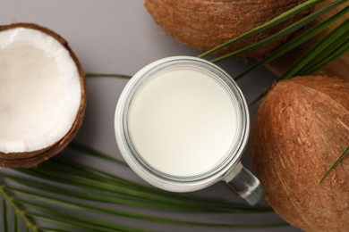 Mason jar of delicious vegan milk, coconuts and leaves on grey background, flat lay