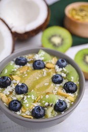 Bowl of delicious fruit smoothie with fresh blueberries, kiwi slices and coconut flakes on white wooden table, closeup