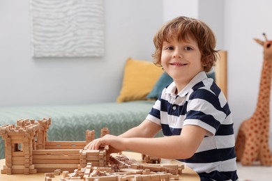 Cute little boy playing with wooden construction set at table in room, space for text. Child's toy