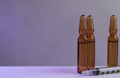 Photo of Brown pharmaceutical ampoules and syringe on white table against color background. Space for text