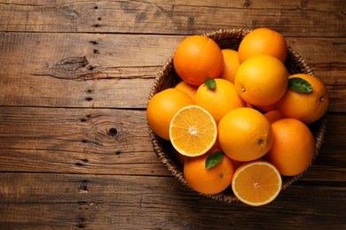 Photo of Many ripe oranges and green leaves on wooden table, top view. Space for text