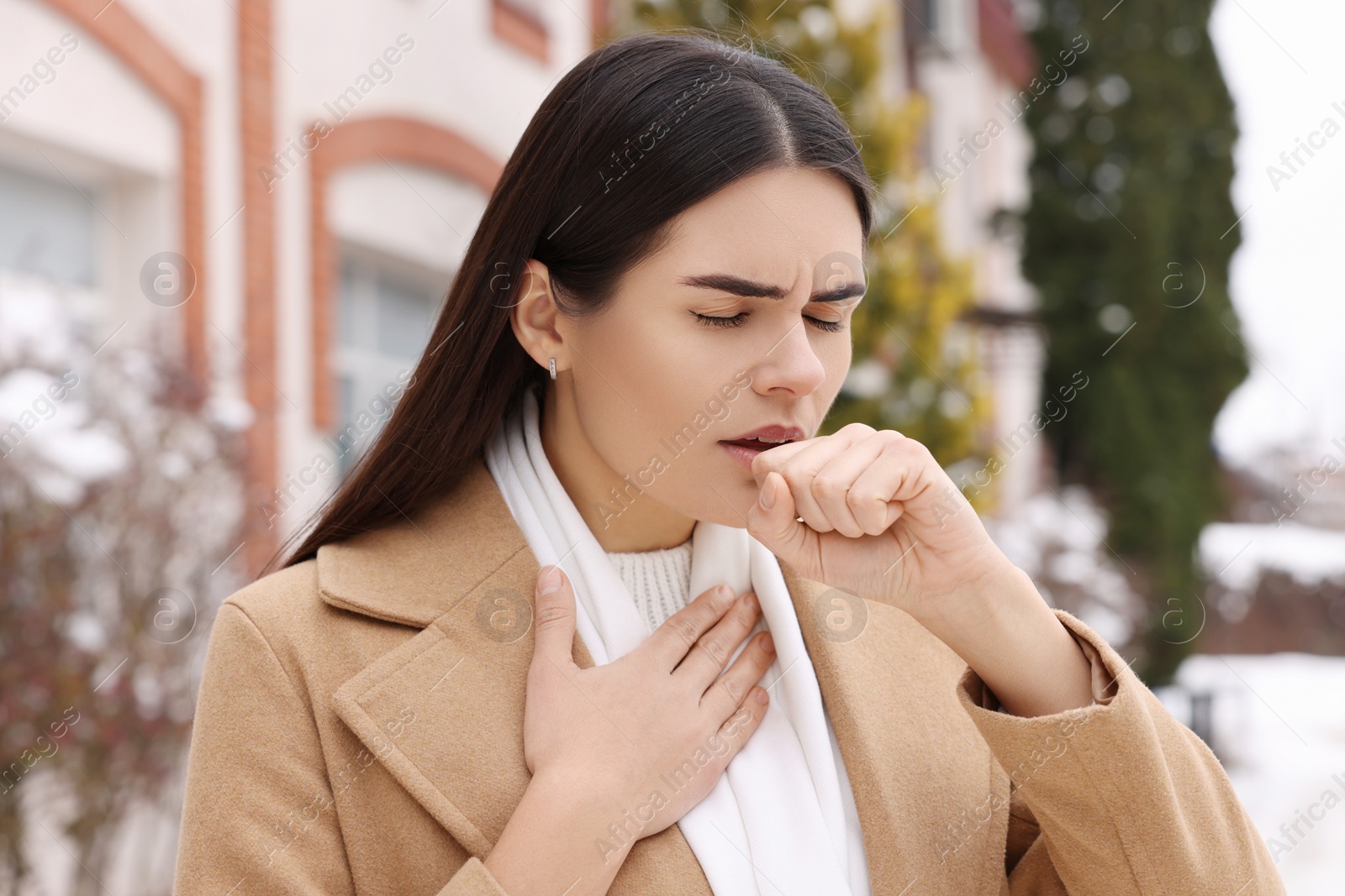 Photo of Woman in coat coughing outdoors. Cold symptoms