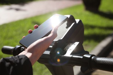 Photo of Man using smartphone to pay and unblock rental electric scooter outdoors, closeup