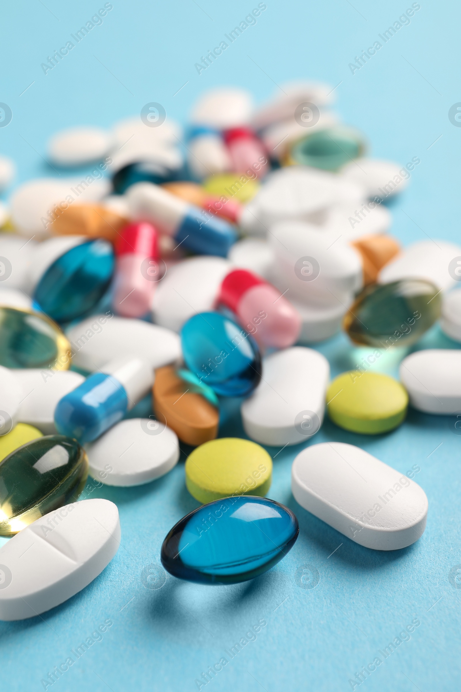 Photo of Pile of different pills on light blue background, selective focus