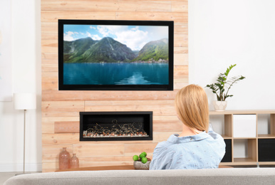 Image of Woman watching TV on sofa in living room with decorative fireplace
