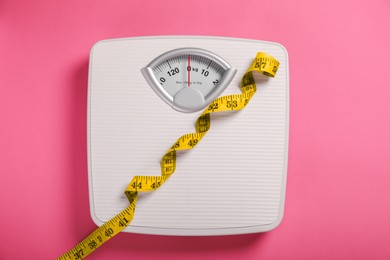 Photo of Weight loss concept. Scales and measuring tape on pink background, top view