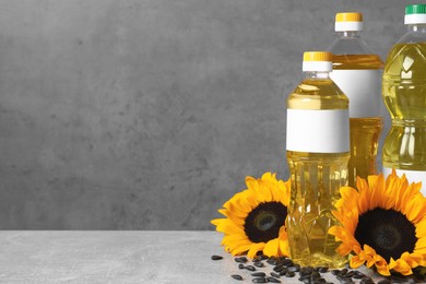 Photo of Bottles of sunflower cooking oil, seeds and yellow flowers on light grey table, space for text