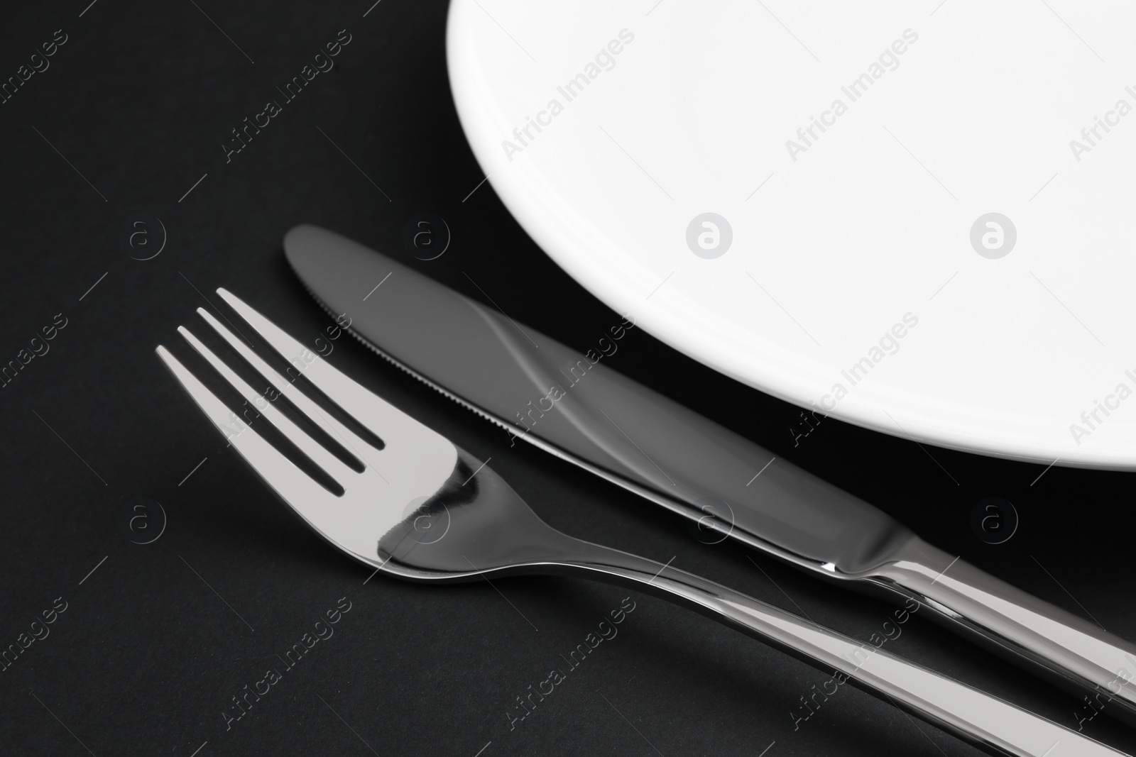 Photo of Clean plate, fork and knife on black table, closeup