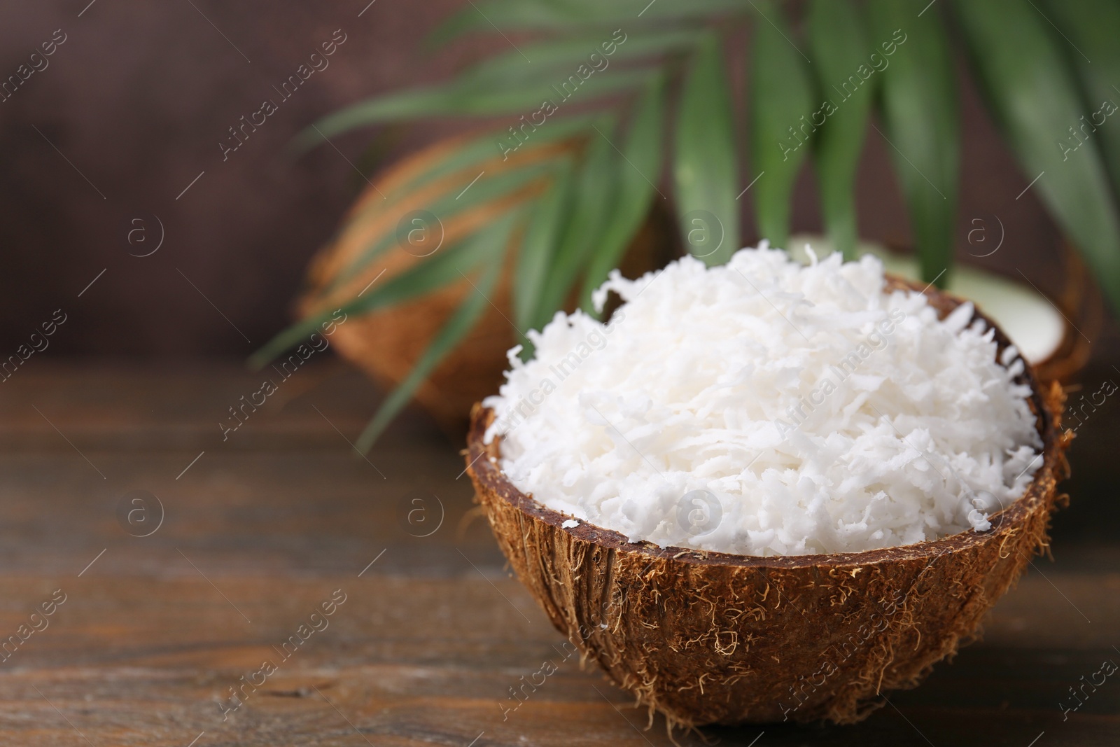 Photo of Coconut flakes in nut shell on wooden table, space for text