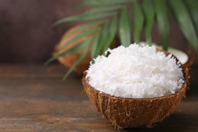 Coconut flakes in nut shell on wooden table, space for text