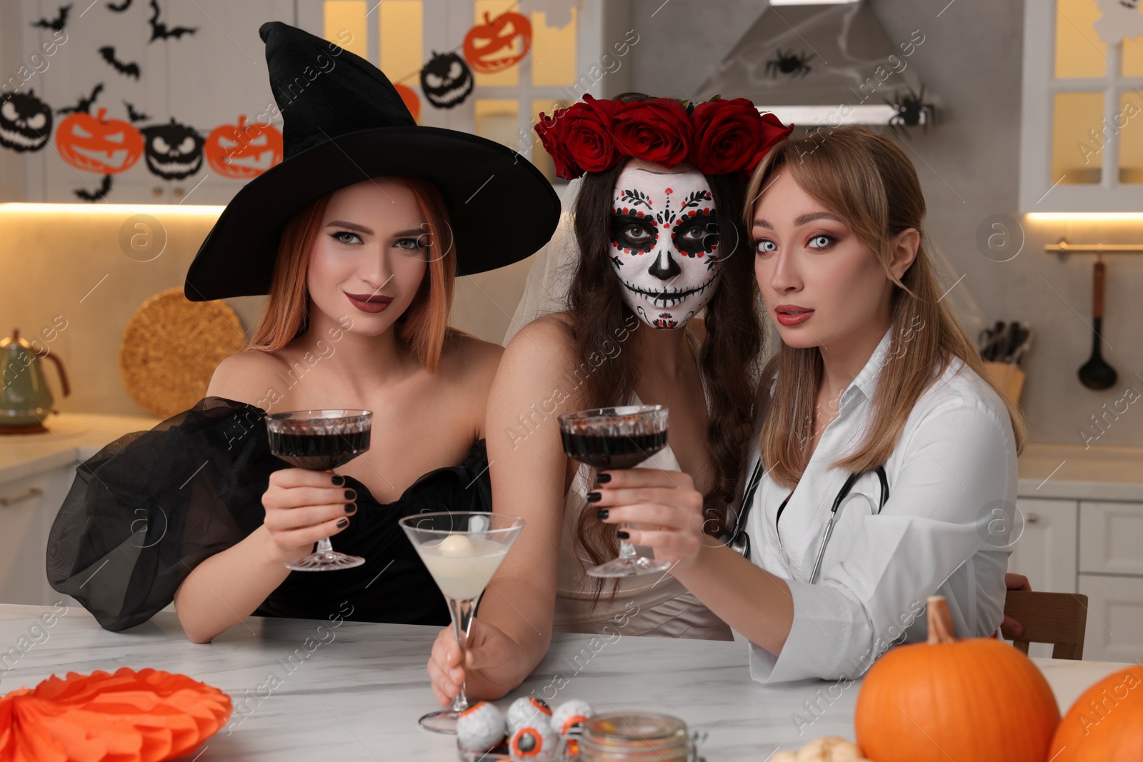 Photo of Group of women in scary costumes with cocktails celebrating Halloween indoors